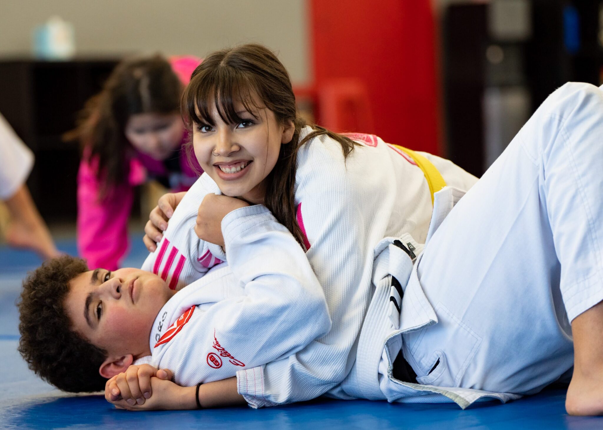 A teen boy and a girl practicing BJJ at Gracie Barra Riverton. The girl is looking at the camera smiling.